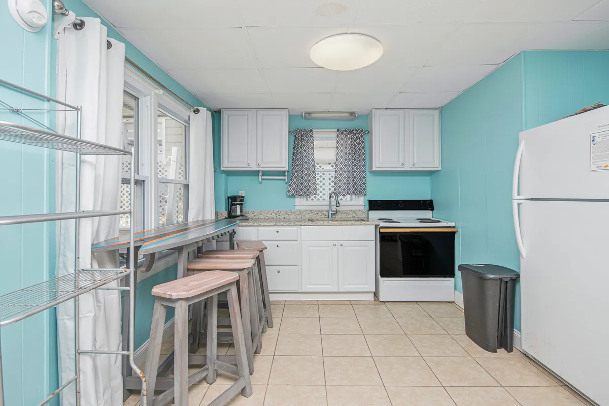 This image showcases a bright, cheerful kitchen featuring a granite countertop, bar stools, ample windows, and kitchen appliances. The open layout and inviting atmosphere make it ideal for group meal preparation and socializing.