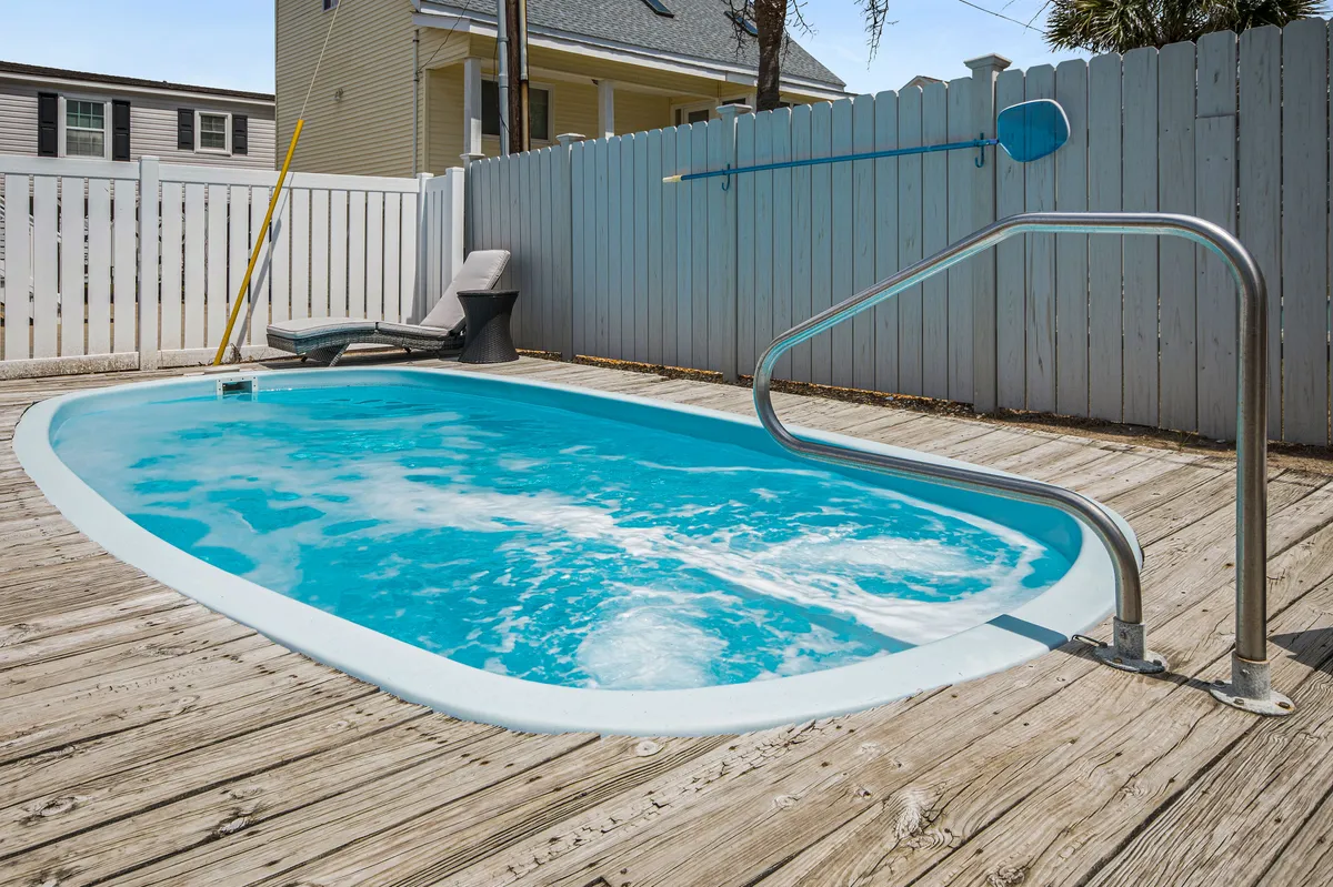 A close-up view of the swimming pool highlights a comfortable lounge chair resting beneath the sun, with the protective fence visible in the background. The ambiance is tranquil, focusing on the inviting water and casual relaxation opportunities by the pool.