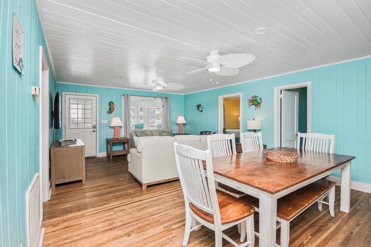 A casual and cheerful living area with a sofa, a colorful wall decor piece, and a dining table set for a shared meal. The room feels bright and sociable, ideal for both special celebrations and daily relaxation.