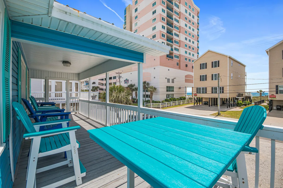 A cheerful exterior scene with turquoise chairs and a table set on a patio, offering a partial view of surrounding buildings. The setting invites relaxation and socializing outdoors, suggesting a pleasant spot to unwind or gather after time by the pool or at the beach.