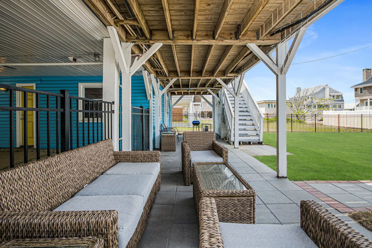 A bright, inviting backyard with a green lawn, surrounded by a safe fence. Wicker seating and glass-topped tables provide a comfortable space for relaxing, socializing, and enjoying outdoor meals. The lawn offers plenty of space for pets or children to play freely and safely.
