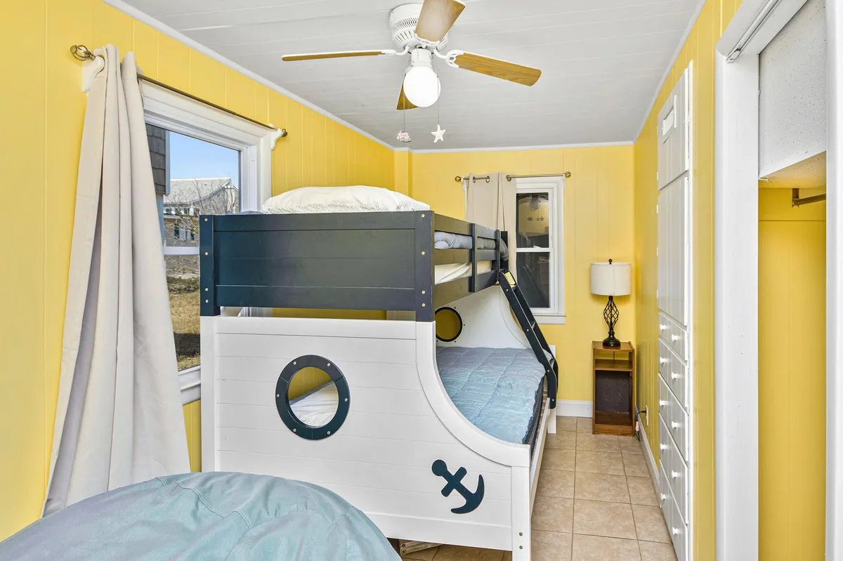A playful bedroom with a bunk bed designed like a boat, yellow walls, a window letting in natural light, and decorative stars hanging from the ceiling. The room exudes coziness and imaginative charm, making it perfect for children or young guests.
