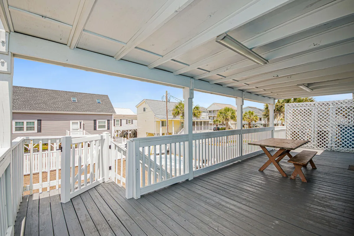 A spacious wooden deck features a large dining table set for a group, with the view extending across neighboring houses. The area is bathed in natural light, ideal for outdoor meals or social gatherings.