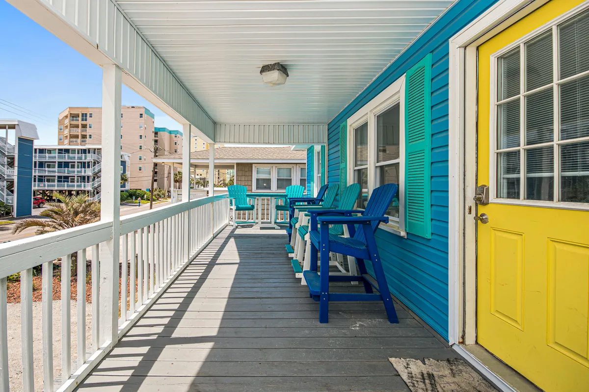 A colorful porch with a bright yellow door and blue Adirondack chairs, set against a vibrant wall. The space is ideal for unwinding after a day at the beach, with ample room for both people and pets to relax and enjoy the fresh air.