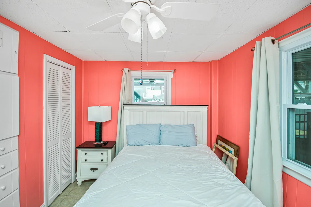 A cozy bedroom featuring coral-colored walls, a bed with light blue bedding, a white nightstand with a lamp, and curtains framing the window. The room looks cheerful yet calm, inviting relaxation and restful sleep.