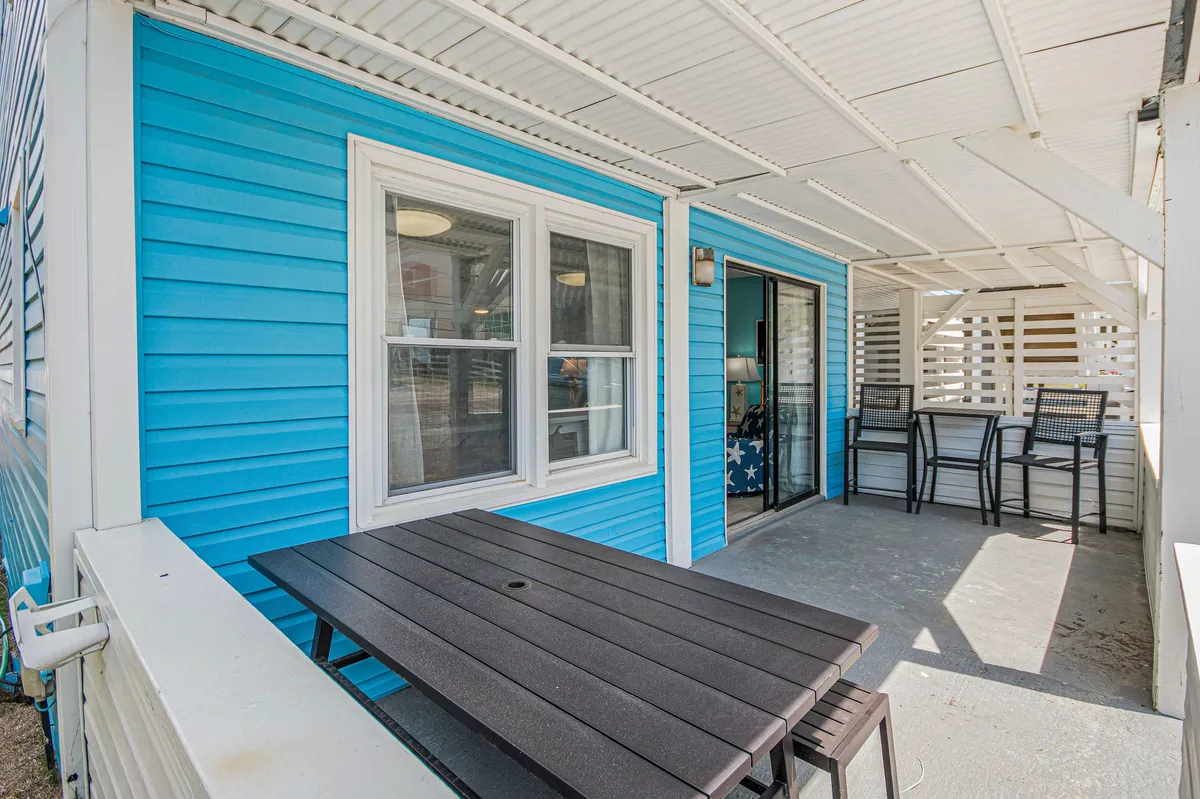 An inviting outdoor table and seating area are set beside the blue siding of the home, hinting at cheerful group meals and relaxed conversations under the sun.