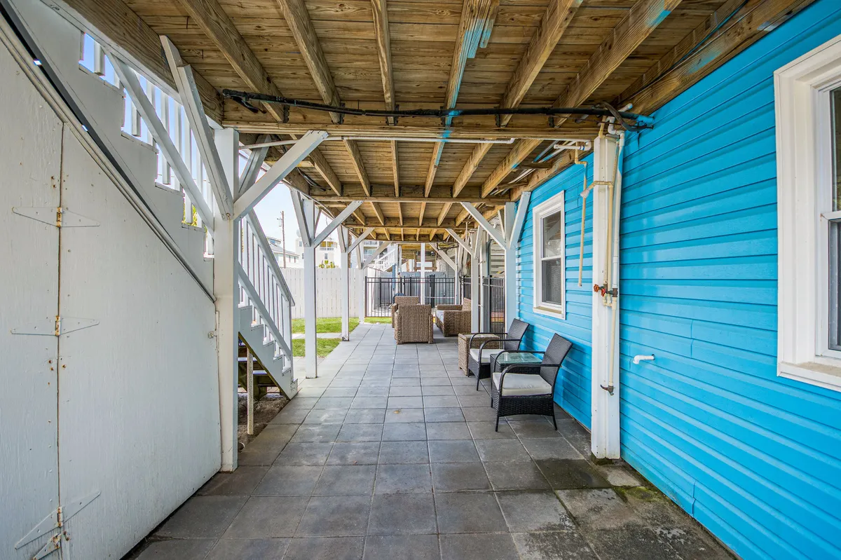 A welcoming outdoor seating area featuring a bright blue wall and wooden beams, complemented by casual seating. The area is bathed in natural light, evoking leisure and outdoor enjoyment, ideal for post-swim lounging or group gatherings.